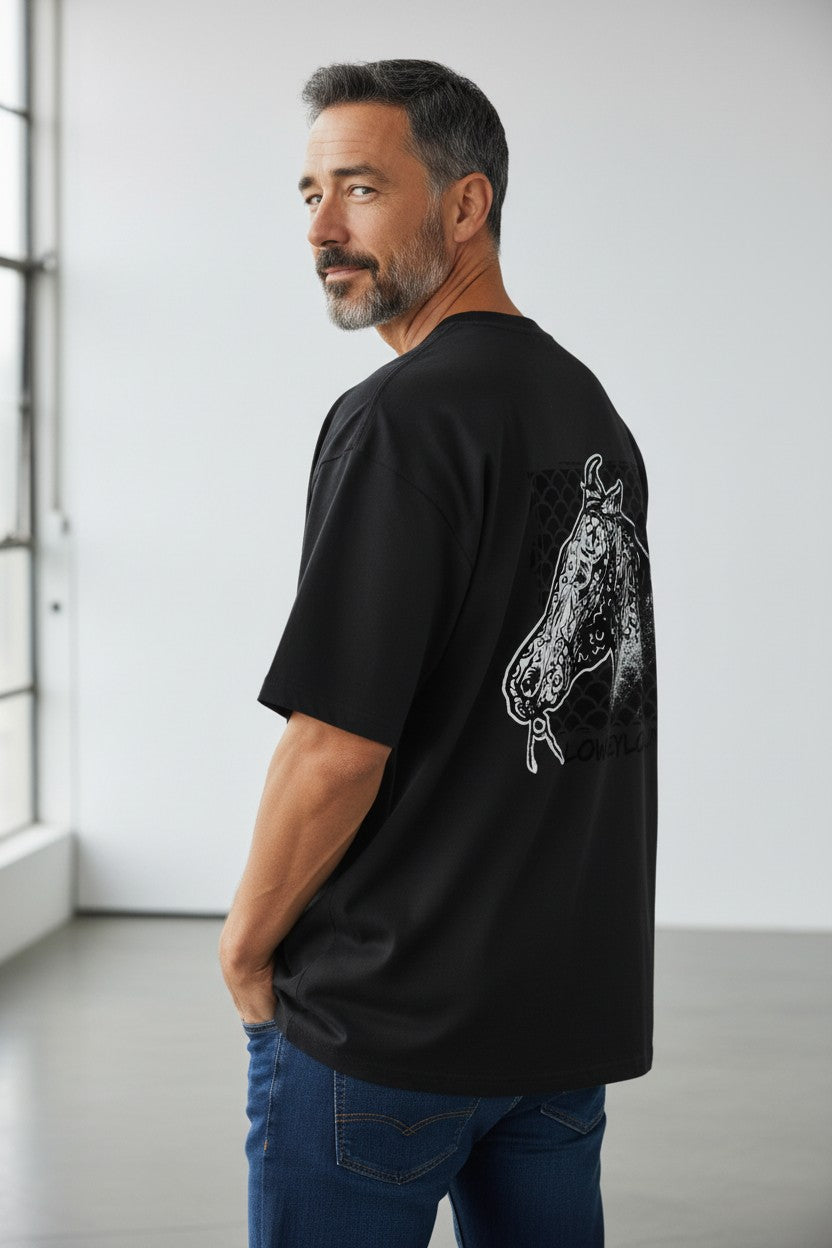 Man wearing a black t-shirt with a graphic design on the back in a minimalistic room.
